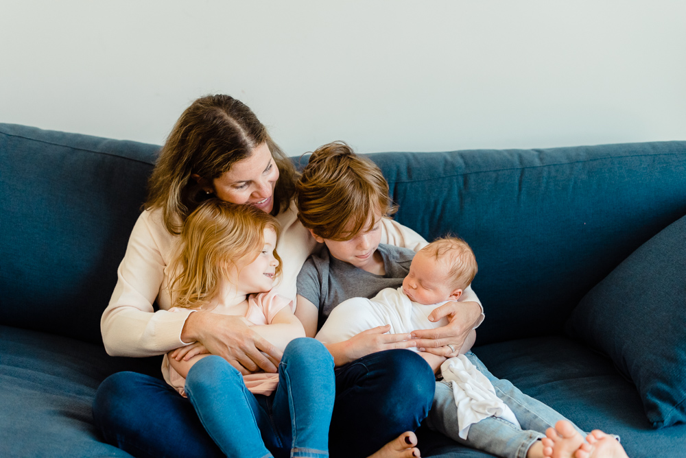 mom, brother and sister sitting on couch holding newborn baby