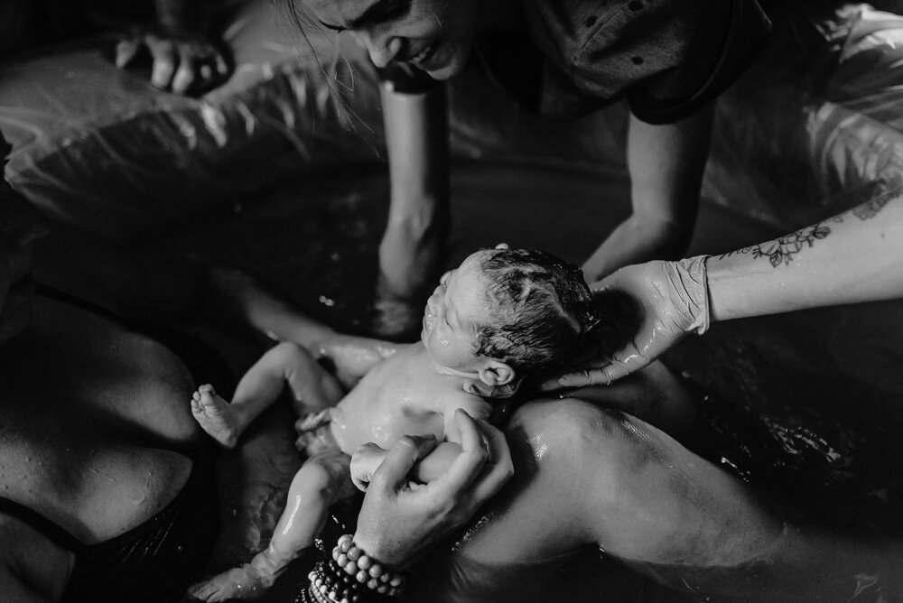 black and white photos of mother and midwife bringing a newborn baby boy out of the birth tub and into mom’s waiting arms.