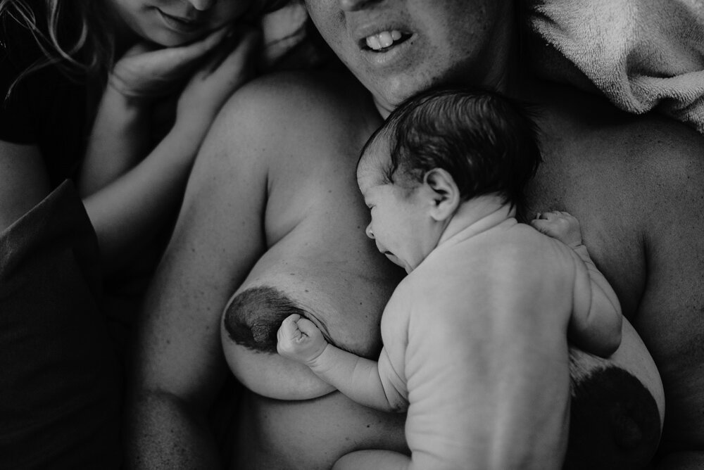black and white image of newborn baby doing the crawl up mom’s stomach to her nipple