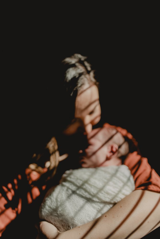 artistic blurred image of postpartum mom holding her newborn baby next to a shadowy alcove