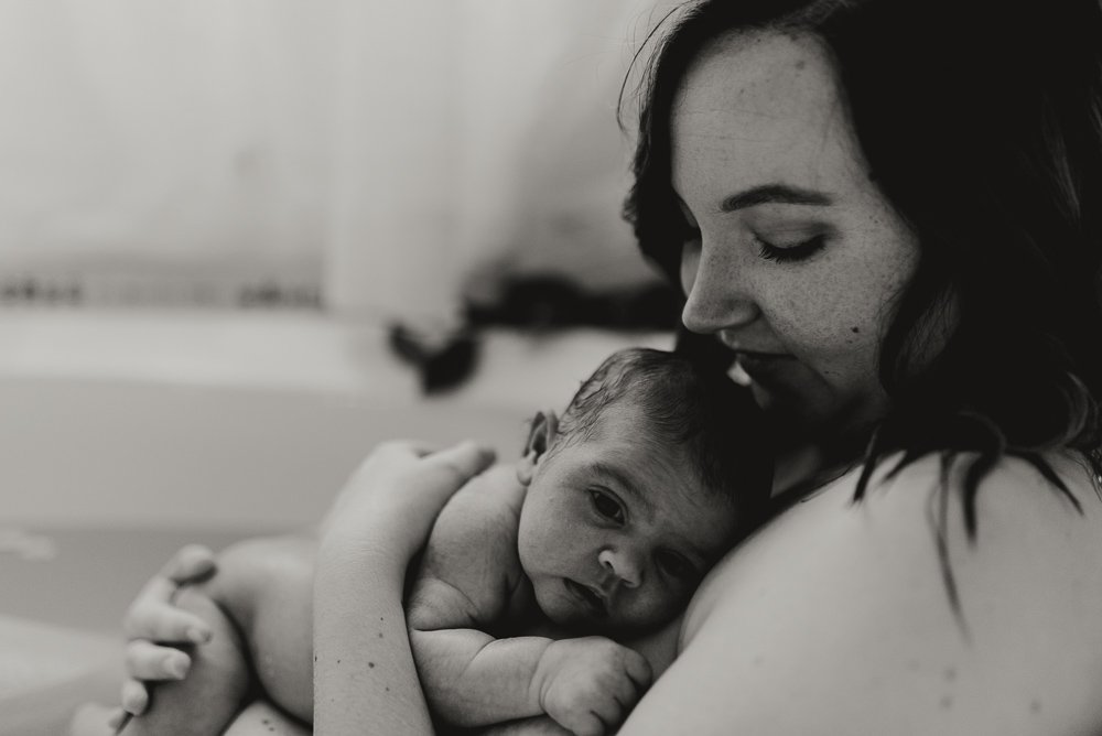 Newborn baby girl naked in the bath with her mom holding her close