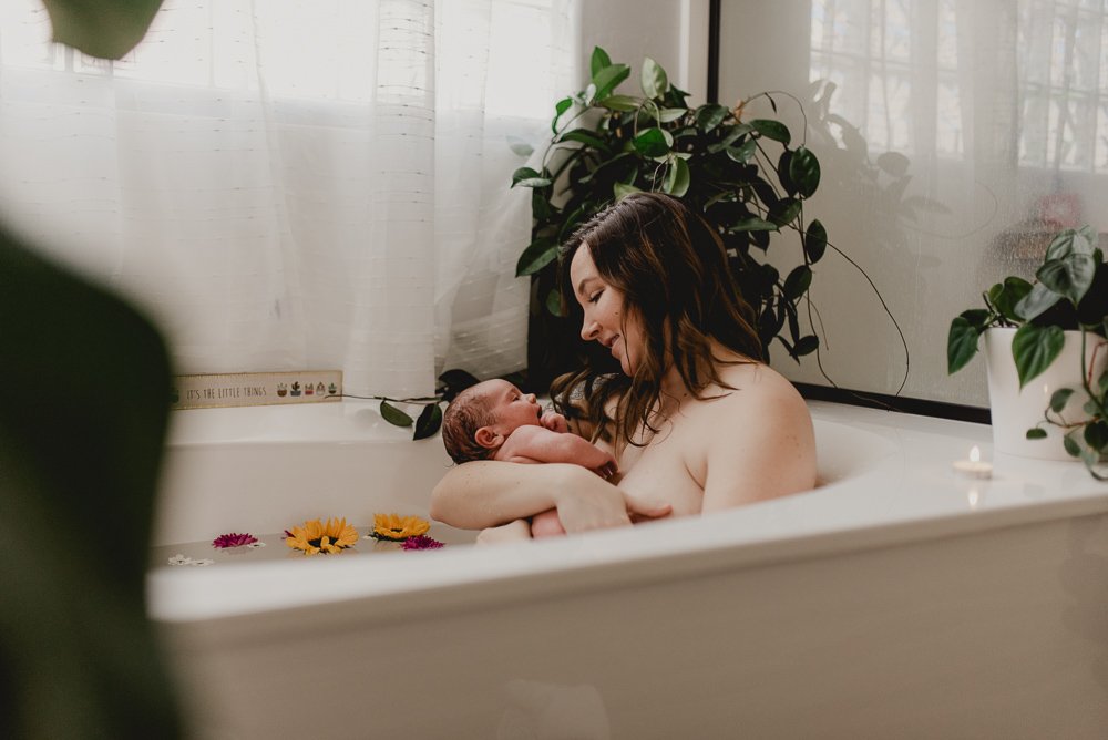 Mom and newborn baby girl snuggling in a floral bath postpartum
