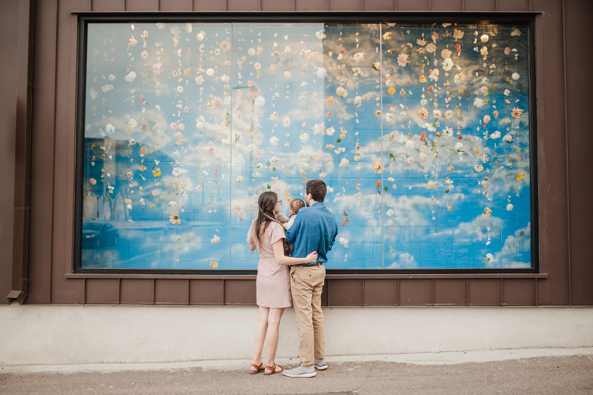 Family of three looking at a blue mural behind glass in downtown Phoenix during family photos