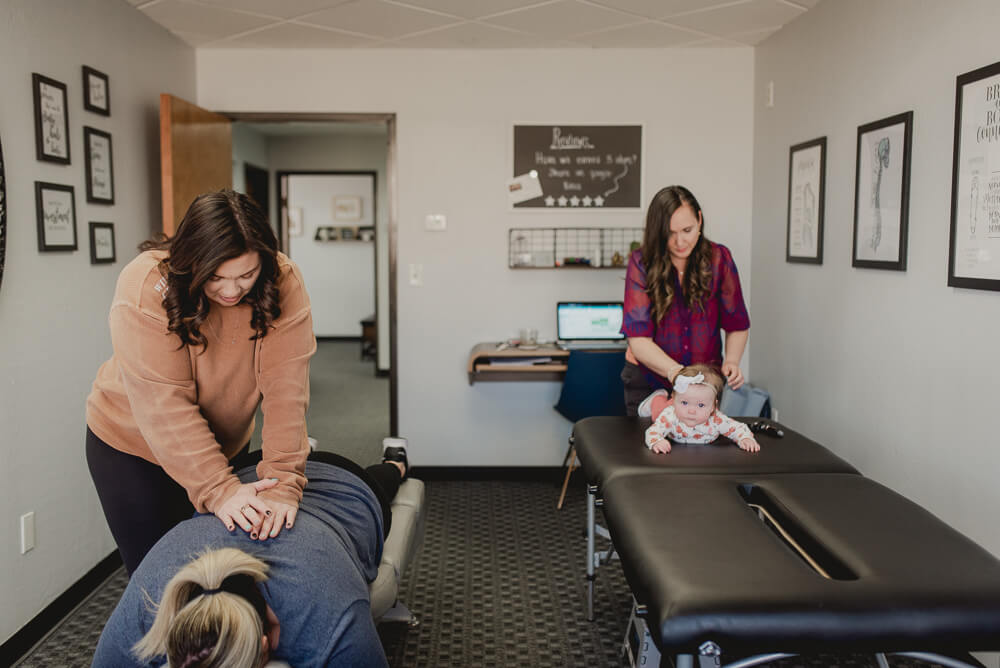 Dr. Erica and Dr. Ashley doing chiropractic adjustments on mom and her baby at Kokua Wellness in Scottsdale