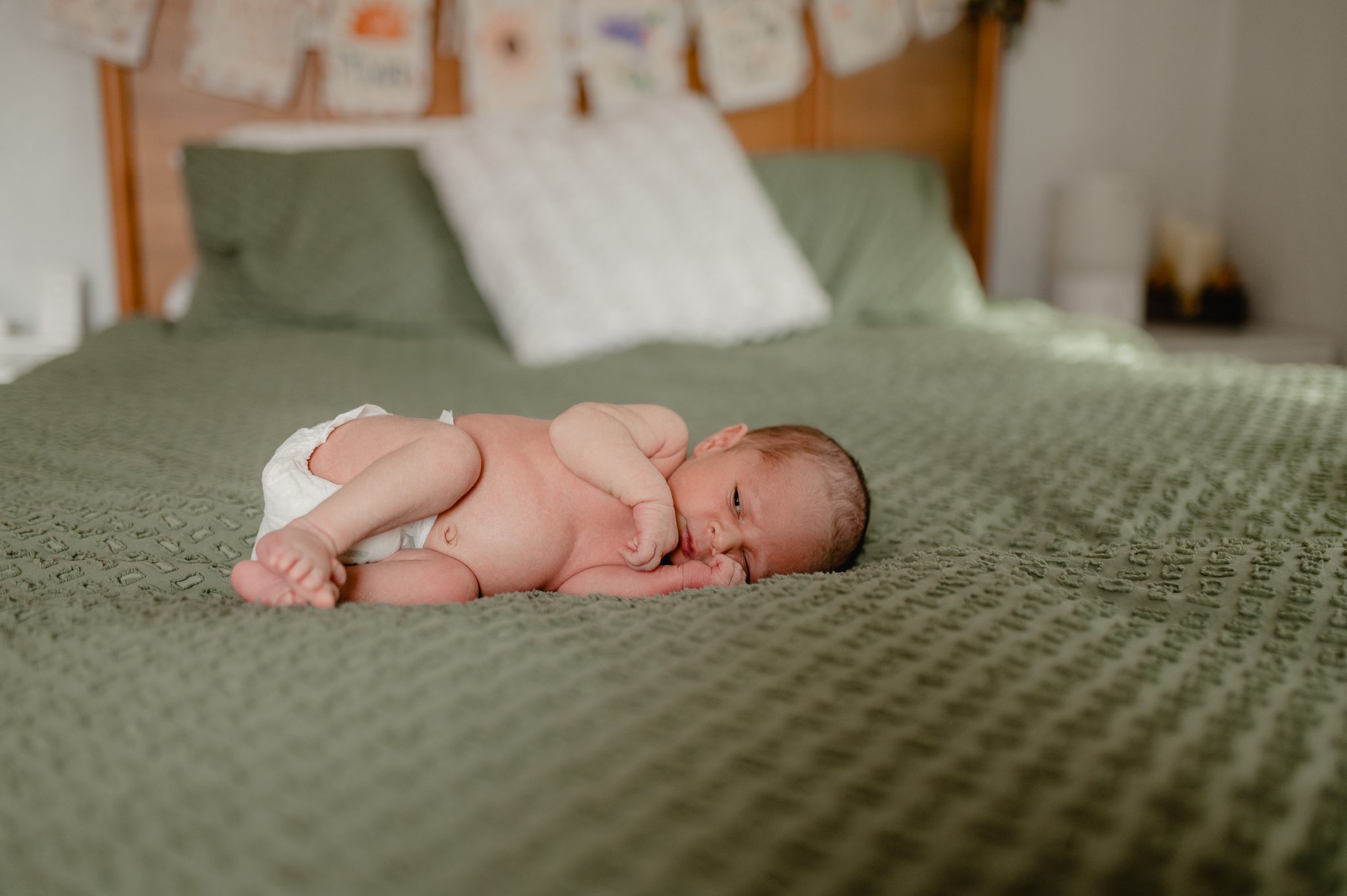 baby boy snuggling naked with only a diaper on the master bed covered with a green bedspread