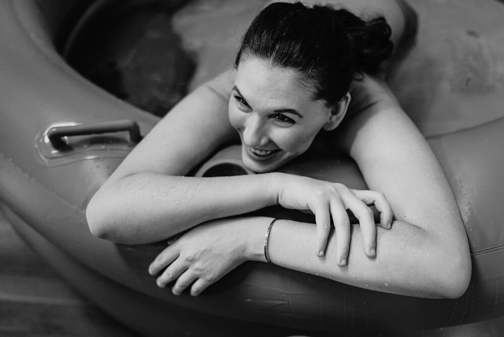 black and white photo of woman laughing while resting between contractions in her birth tub