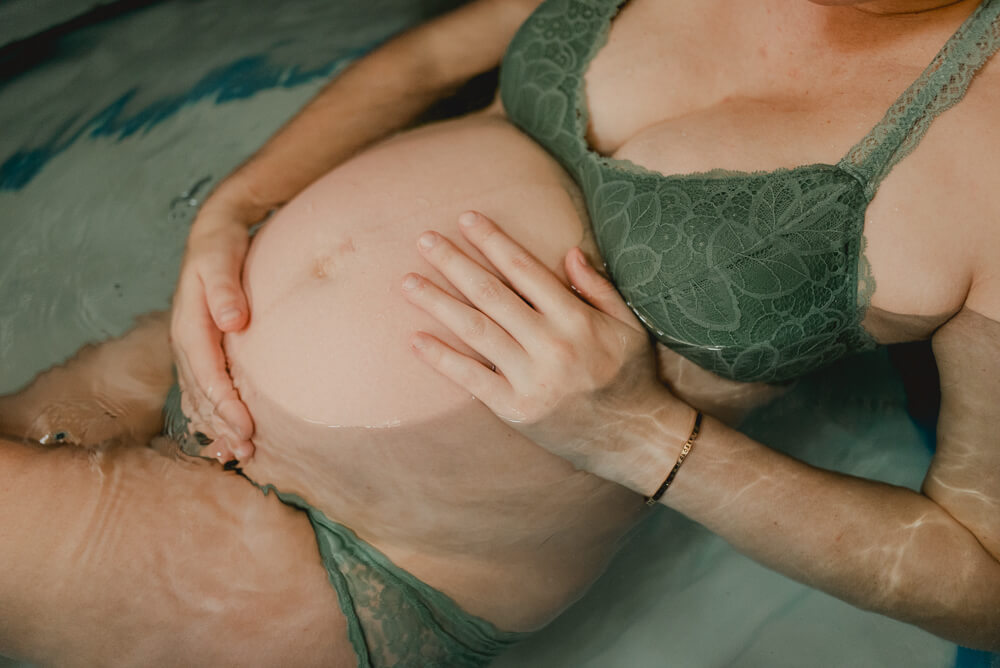birthing woman holds her pregnant belly while laying in her birth tub