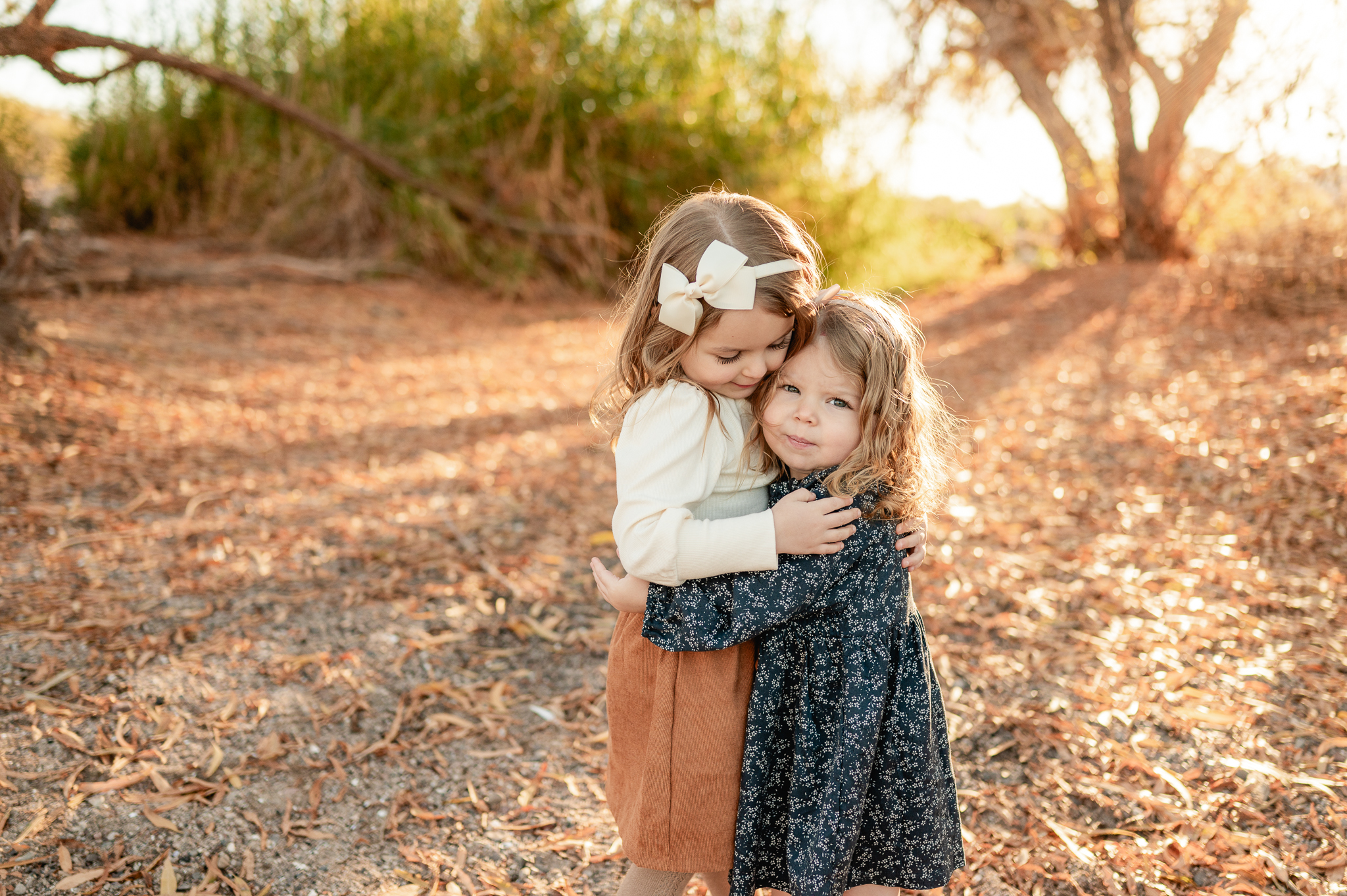 5 year old and 3 year old sisters hugging in a field wearing Cricket and Ruby boutique dresses