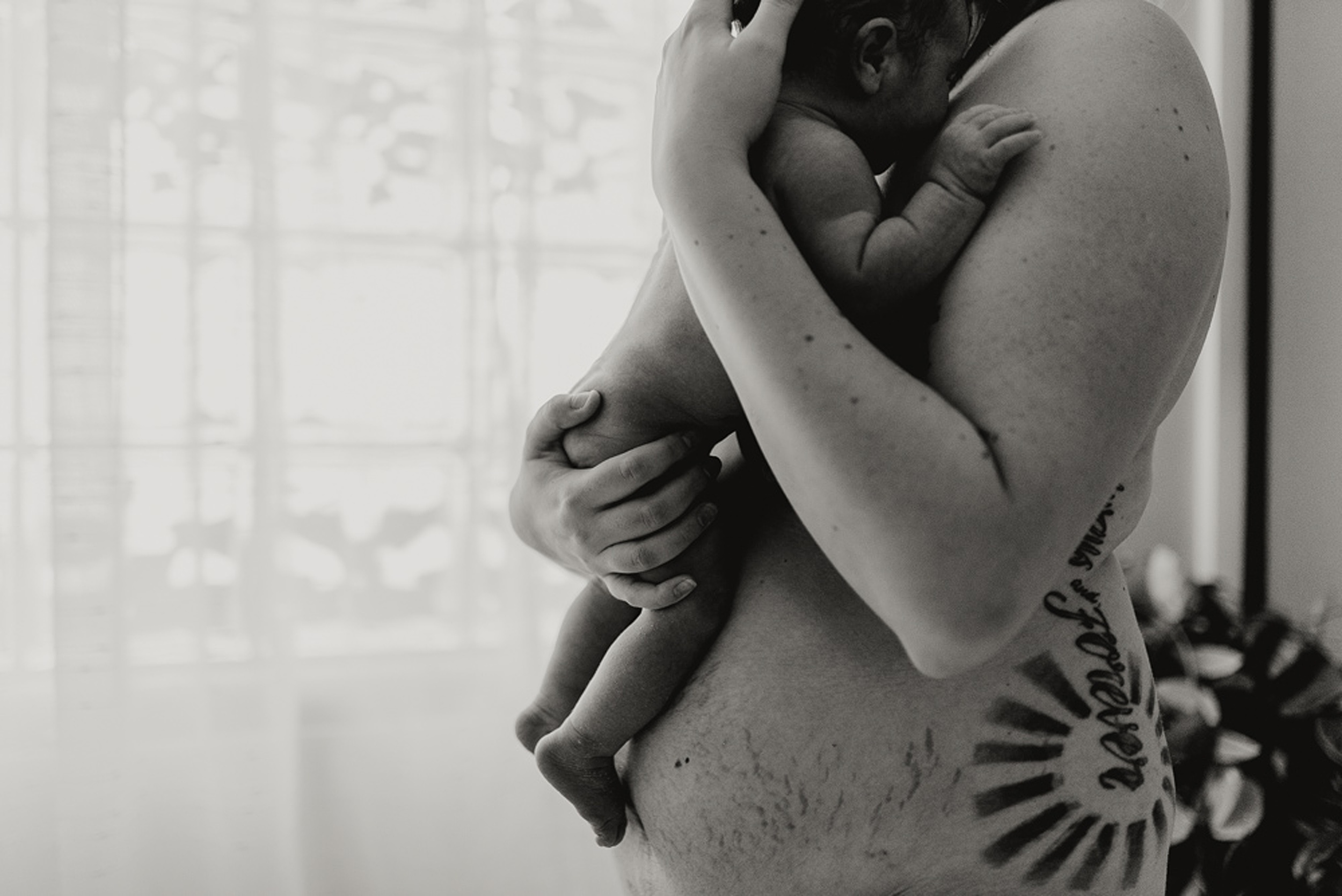 A mother stands in a bathroom cradling her newborn baby against her naked body after using family first midwifery