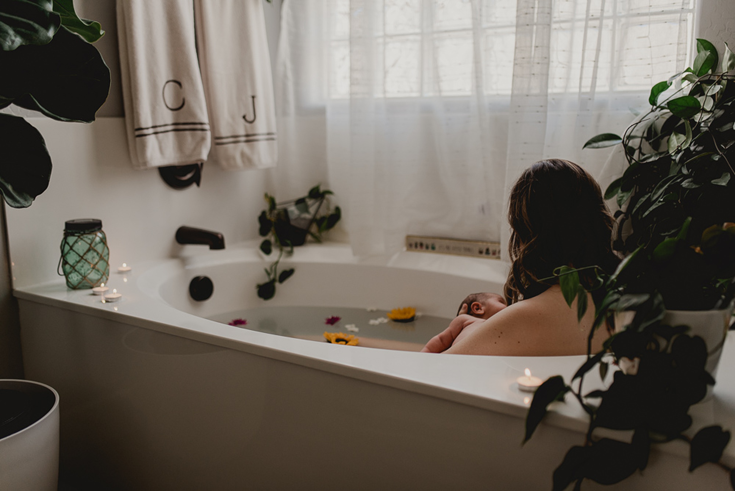 A look at a mom breastfeeding her newborn baby while taking a bath with houseplants under a window