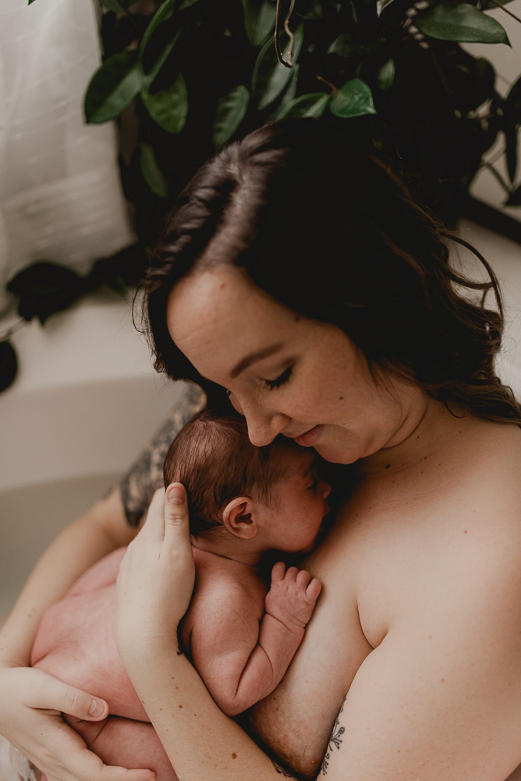 A new mom sits in a bathtub cradling her newbron baby against her chest thanks to family first midwifery