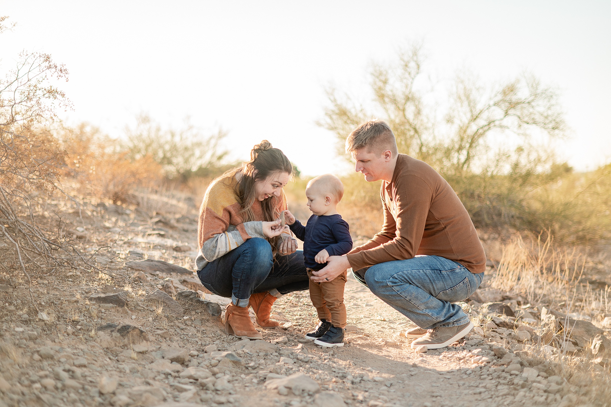 A mom and dad squat and explore a desert path with their toddler son before visiting scottsdale yoga studios