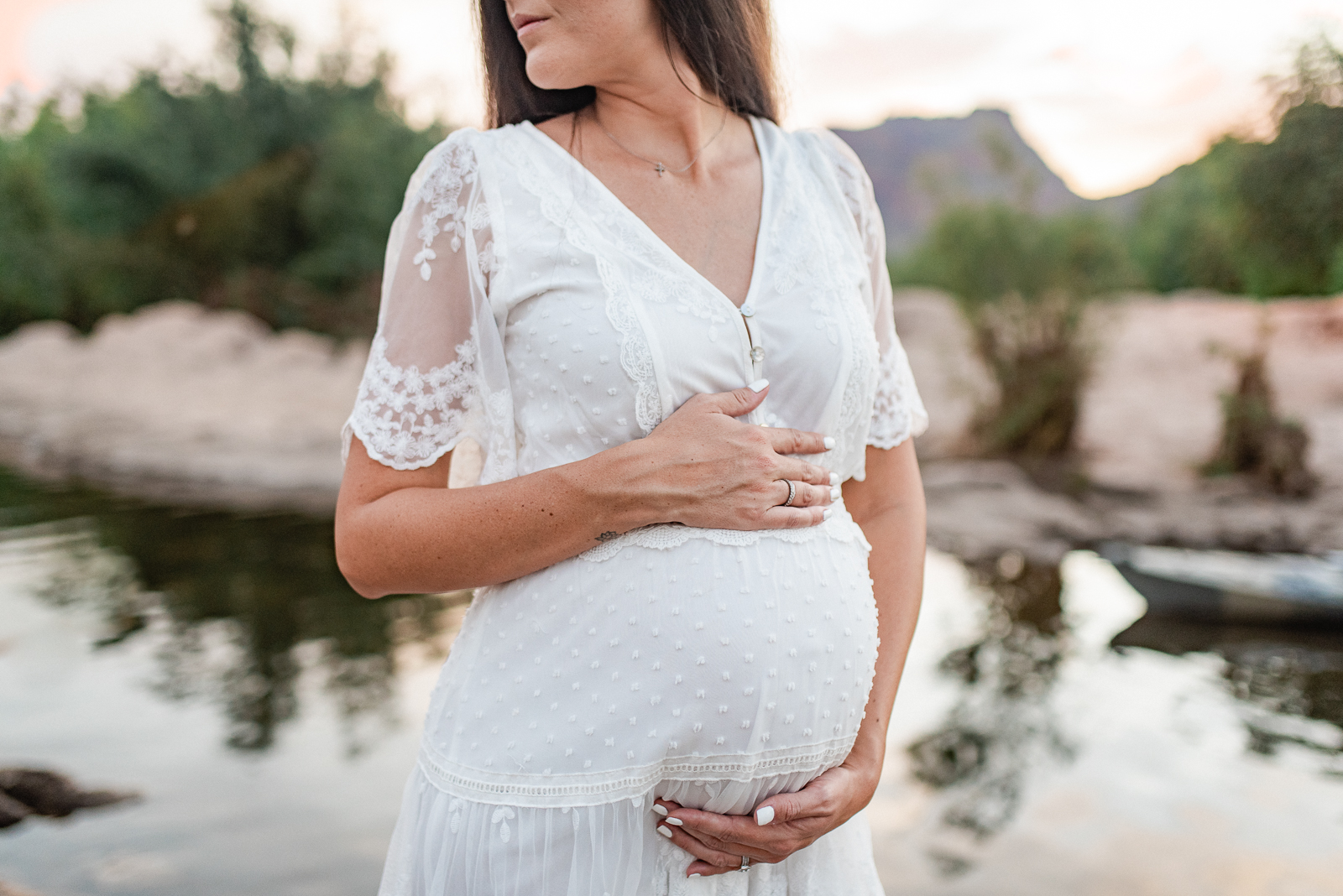 Pregnant woman holds her hands around her belly while looking to the side surrounded by the glowing light and Phoenix mountains