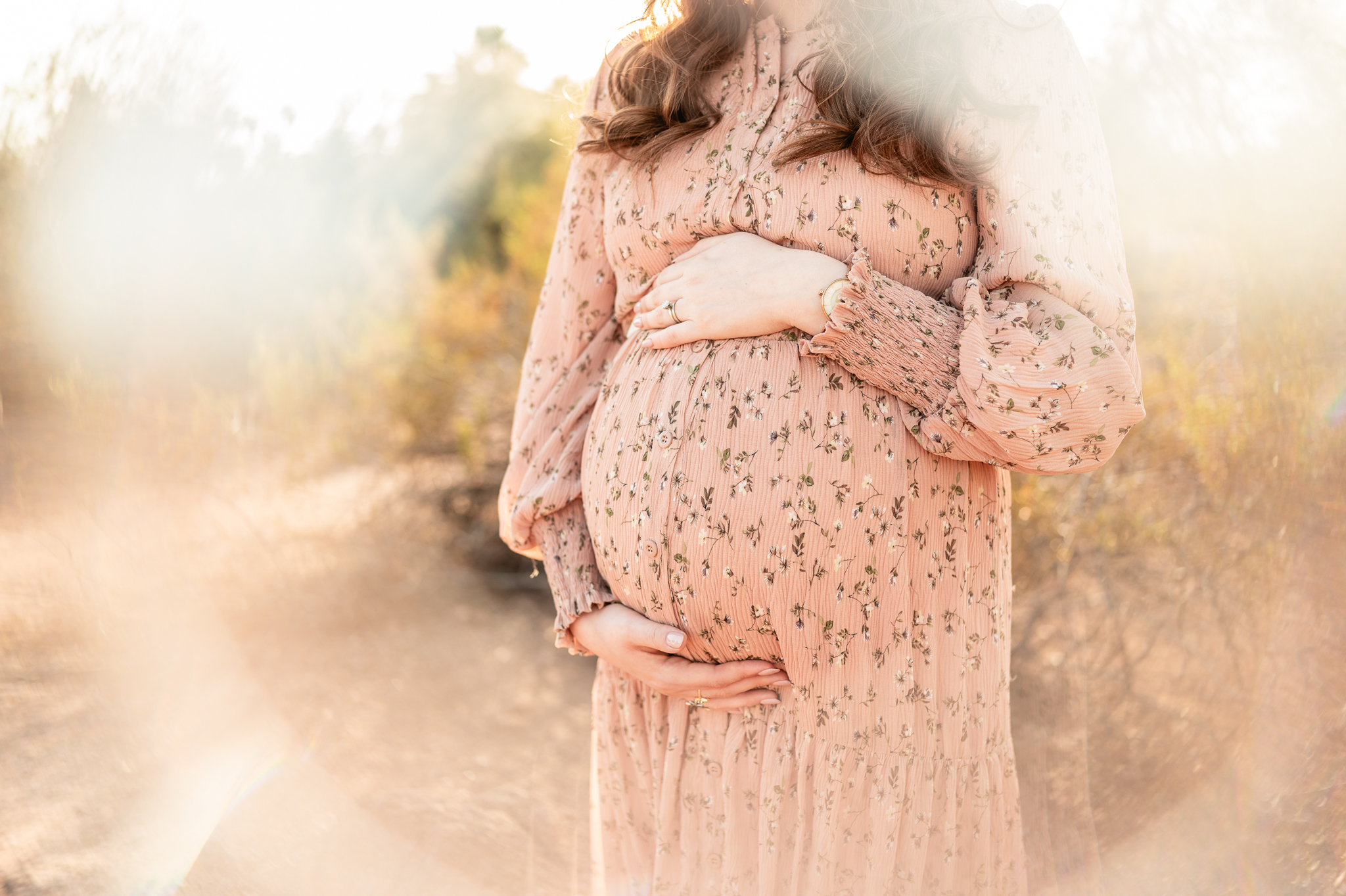 mother caresses her pregnant stomach while wrapped in soft light outdoors