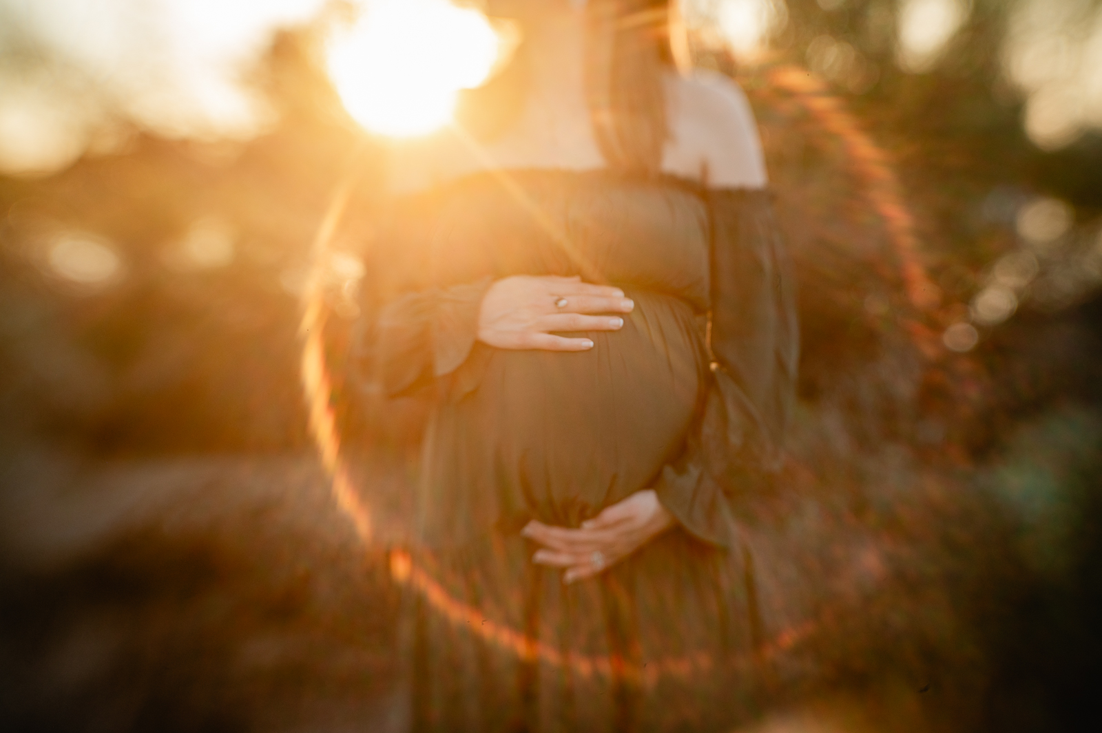 Phoenix pregnant woman holding her baby in green maternity dress with sunflare