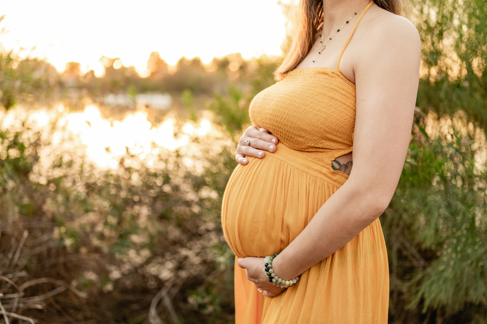 pregnant mama holding her tummy with a mustard yellow maternity gown with sunlight shining behind her