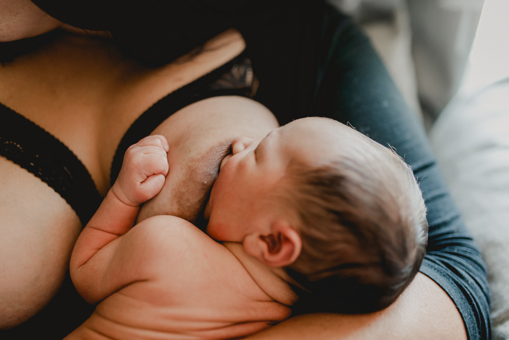 newborn baby boy breastfeeding while he clutches mom's breast