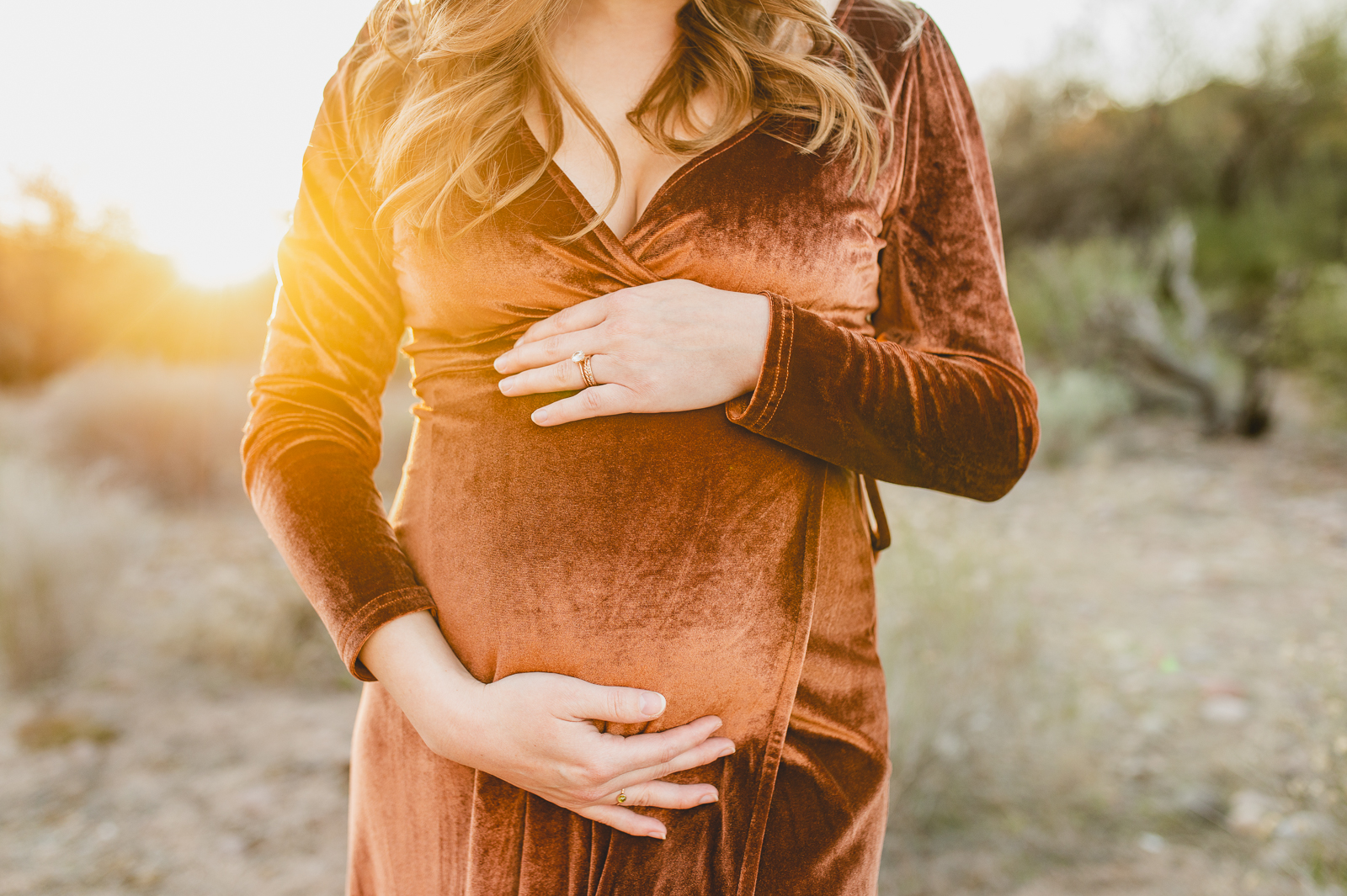 pregnant woman wearing a velvet maxi wrap maternity dress with sun glowing behind her