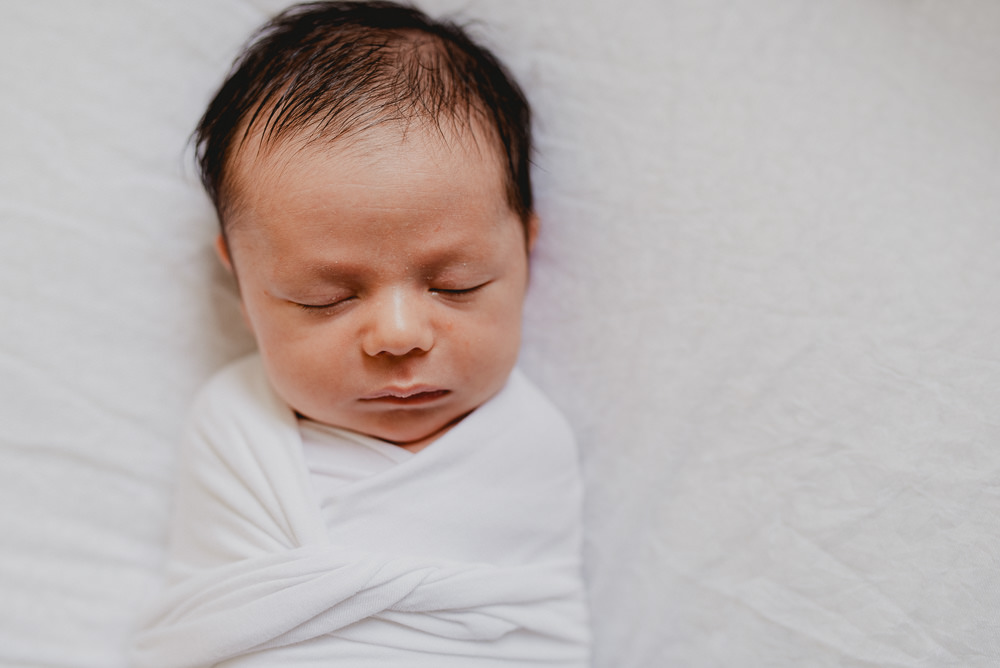 A newborn baby sleeps while wrapped in a white swaddle thanks to Bloom Reproductive Institute