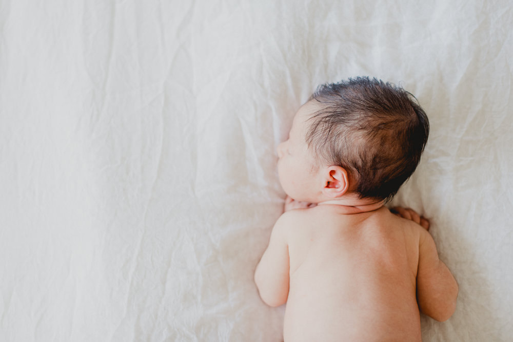 A newborn baby with dark hair sleep on its tummy thanks to Bloom Reproductive Institute