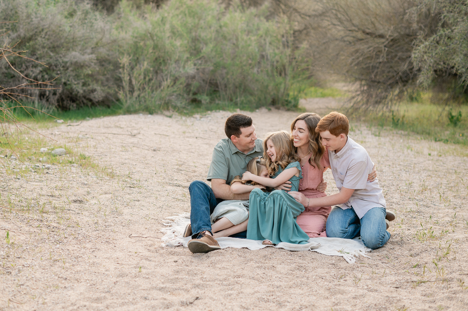 family of five snuggling in pastel clothes among the trees and desert at Butcher Jones Recreation