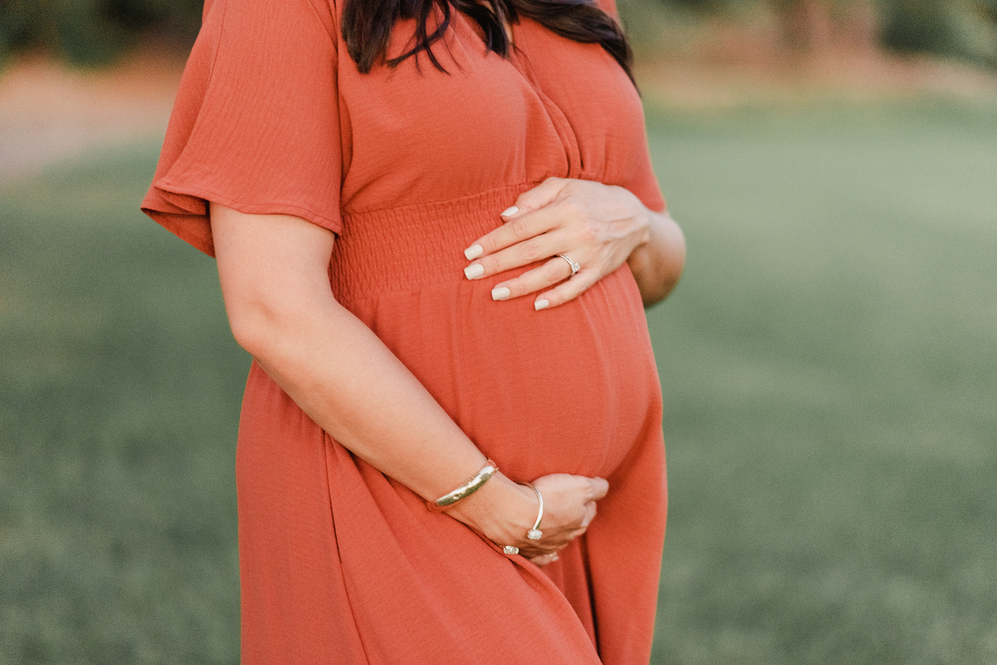 pregnant mama holds her belly in an orange dress at a park in Phoenix at sundown