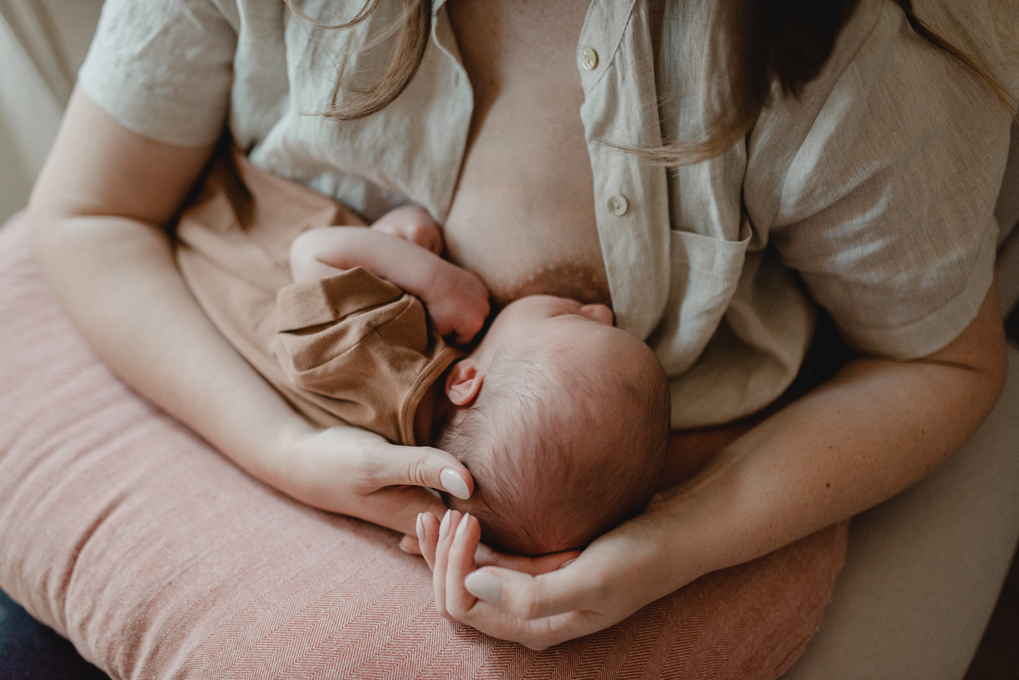 mom nurses her newborn baby in her nursery using a soft pink nursing pillow