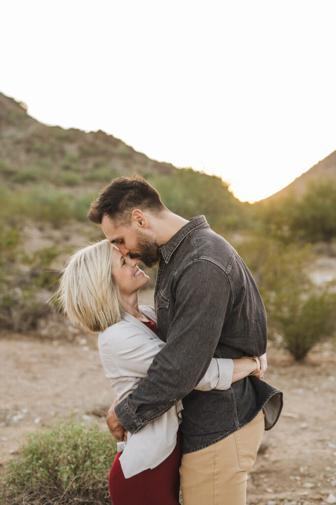 wife looking up at husband who is holding her in his arms kissing her forehead with the golden Scottsdale mountains behind them as the sun sets